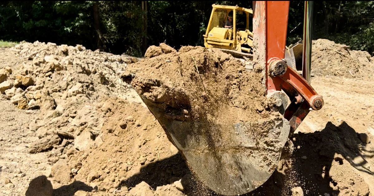 Excavator digging a dirt mound at a construction site, with a yellow machine in the background.
