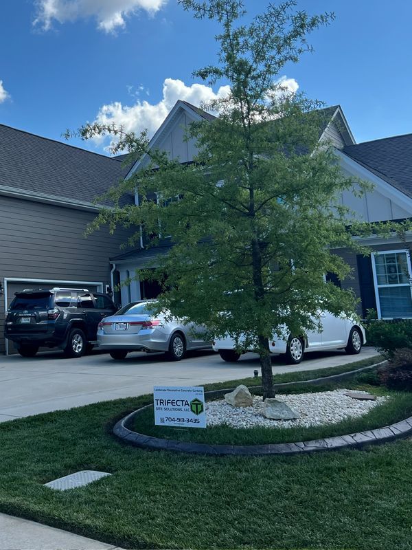 Suburban house frontage with driveway, parked cars, and a small tree in a landscaped yard.