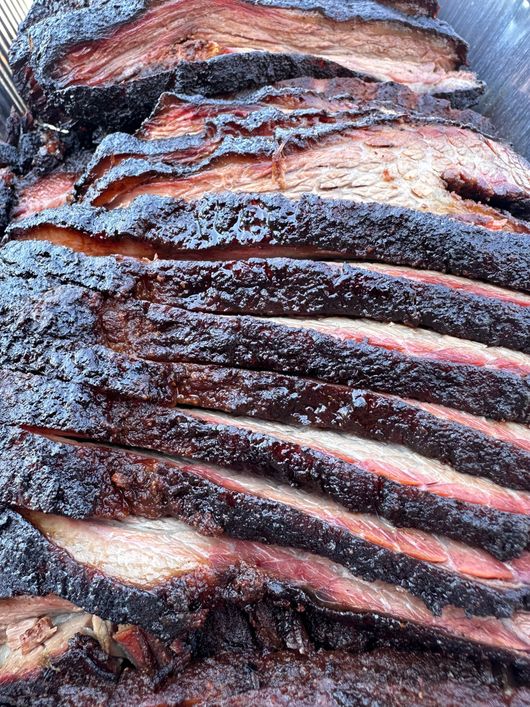 Slices of smoked, charred meat with a dark crust and pink interior close-up