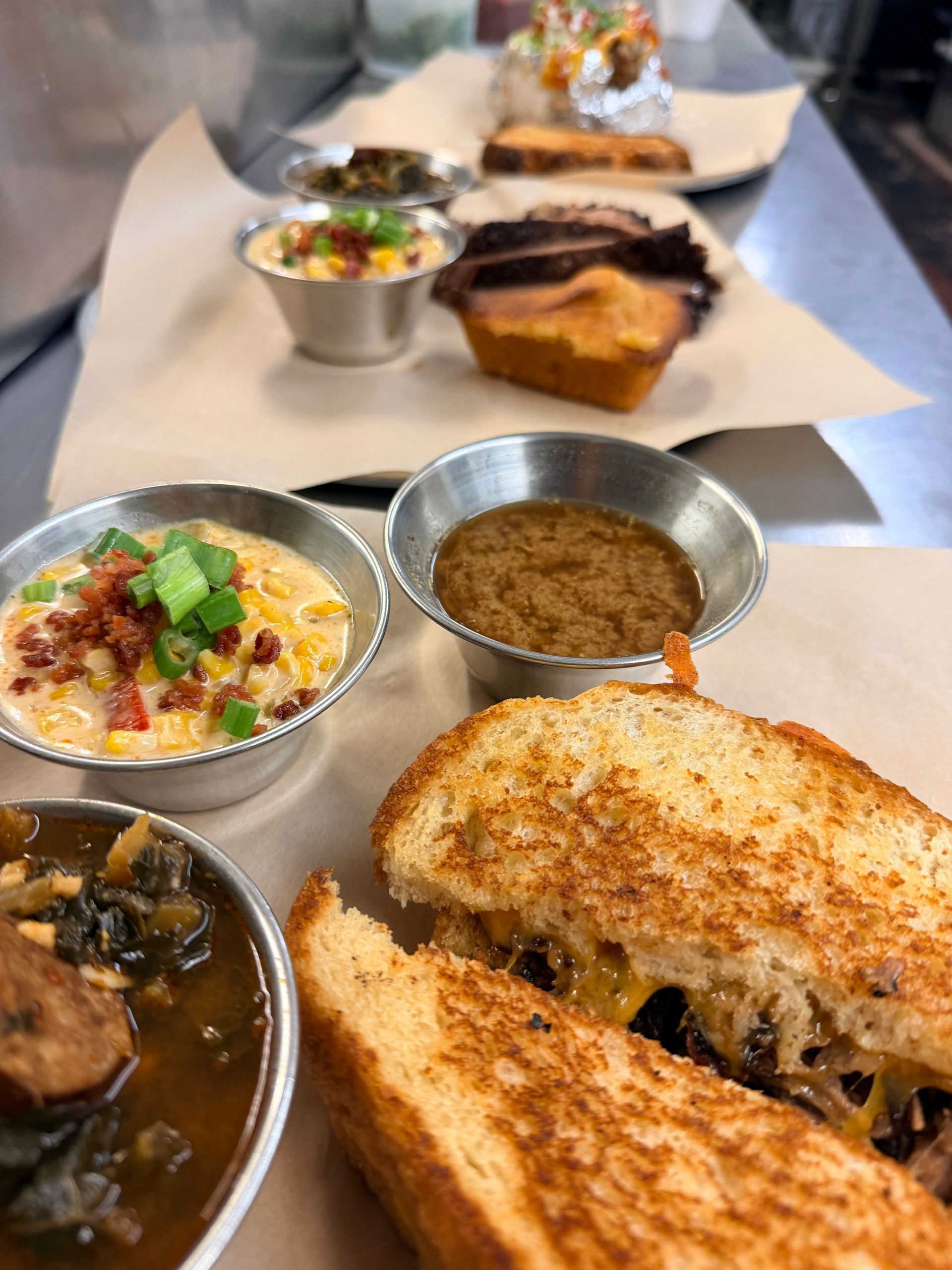 Assorted small dishes and grilled sandwich on a table, with a plated dessert in the background
