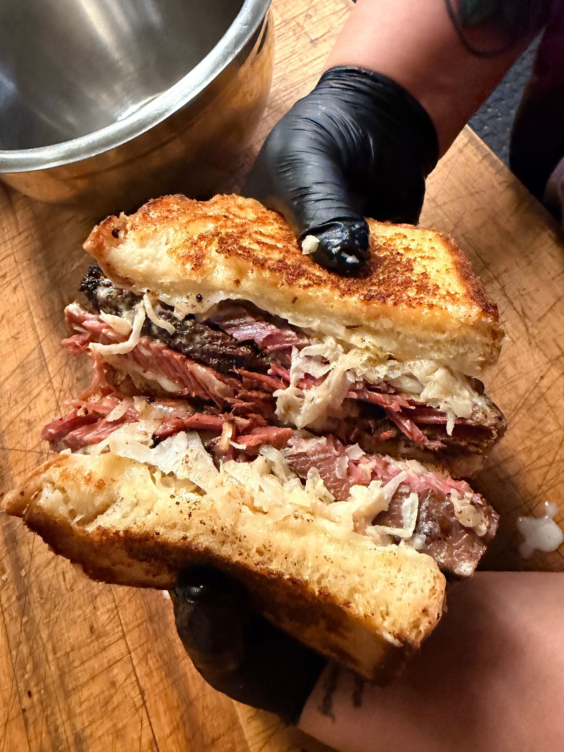 Hands holding a toasted sandwich stuffed with shredded meat over a wooden table