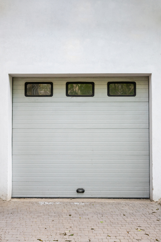 A white garage door with three windows and a brick driveway.