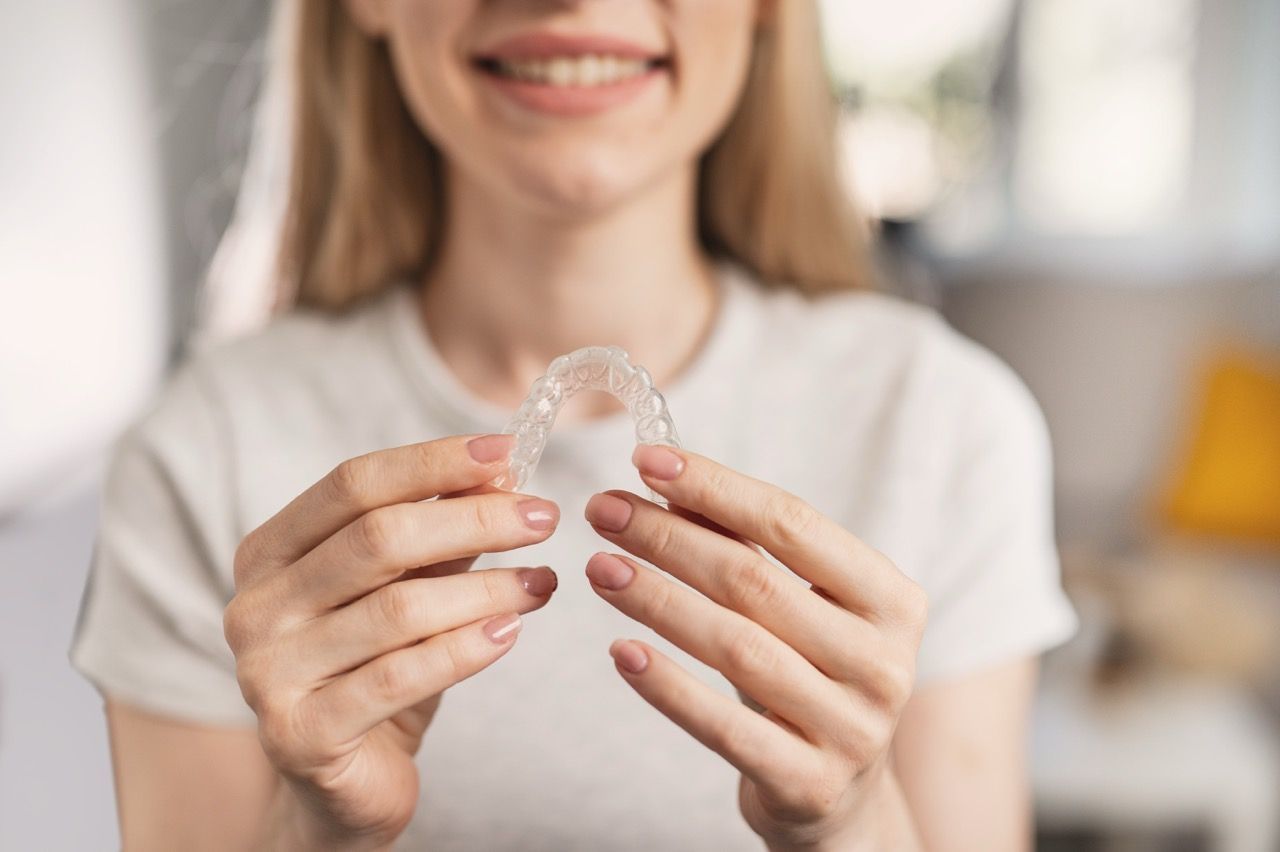 Person holding a clear dental aligner in front of a blurred indoor background