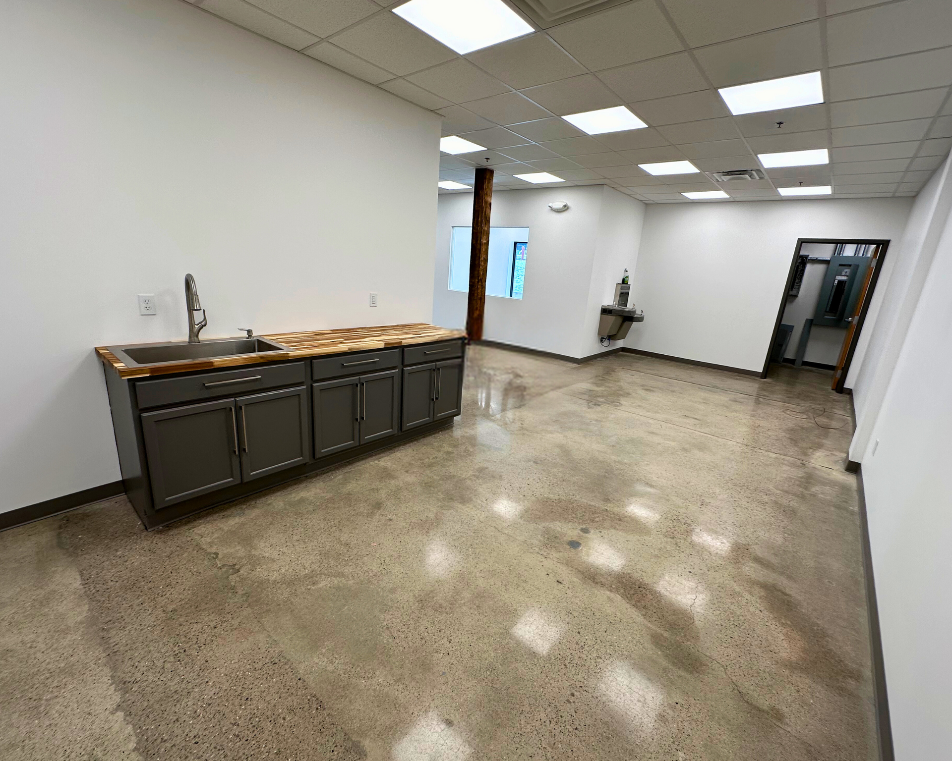 Empty office space with gray cabinets, sink, and concrete floor. White walls and ceiling.