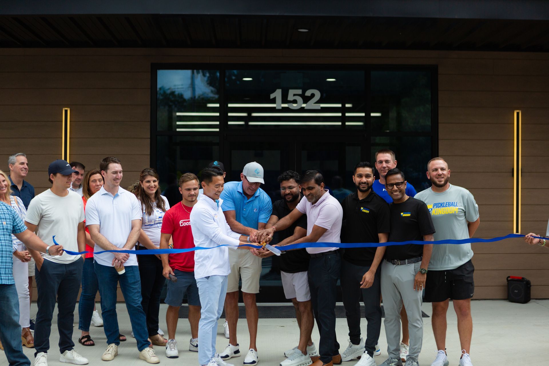 Group cutting a blue ribbon in front of a building with