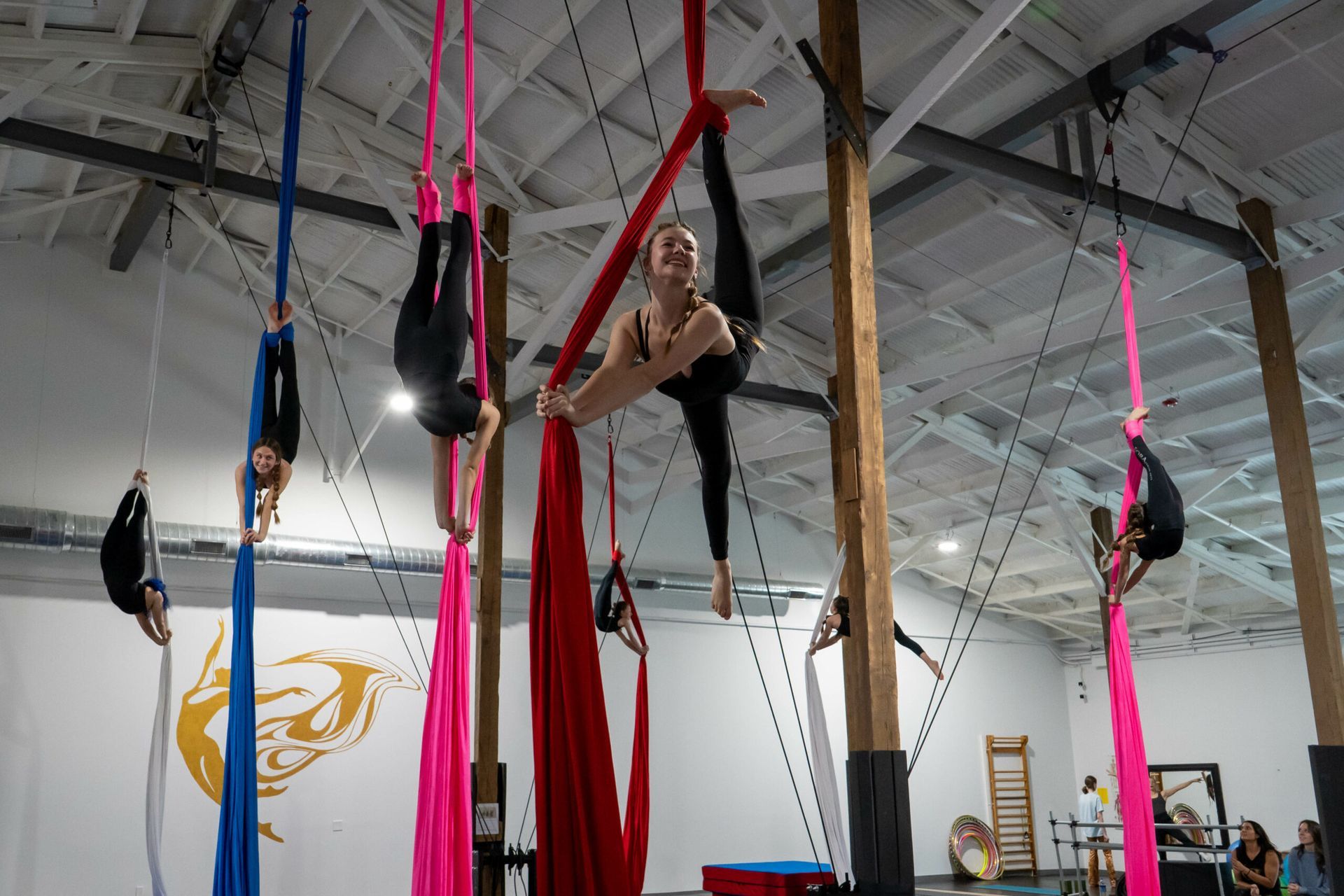Aerial silks performers in a large studio. Various poses on colorful fabric hanging from the ceiling.