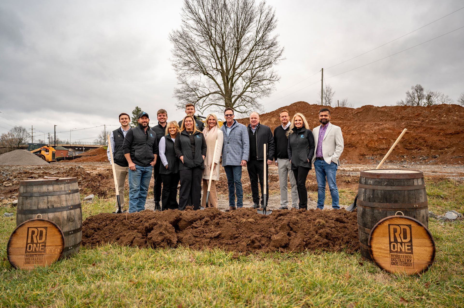 A group of people are standing in a field next to barrels.