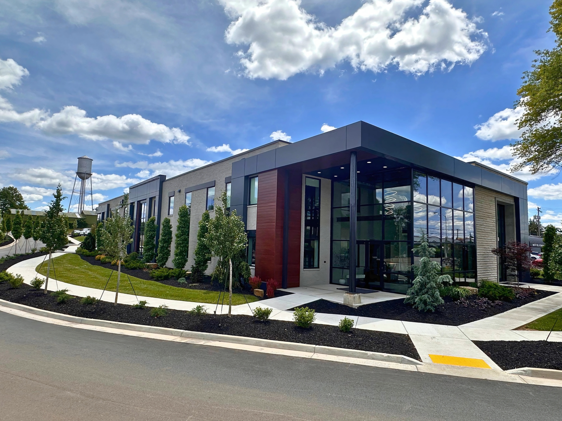 Modern office building with glass windows, gray facade, and landscaped grounds under a blue sky.