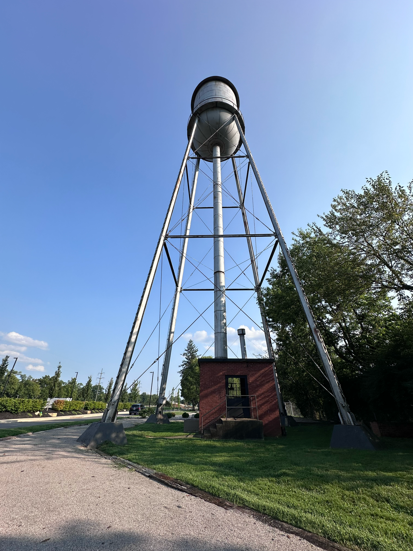 Water tower with silver tank on metal frame, brick base, against blue sky.