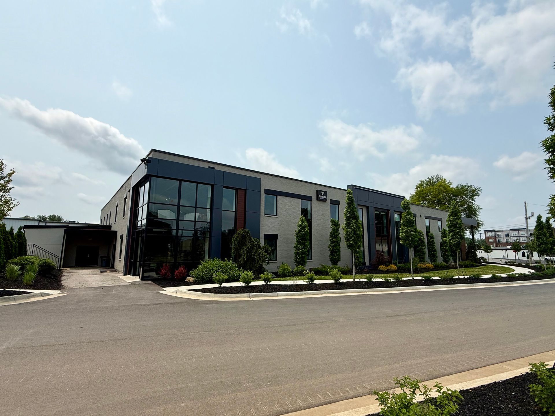 Modern, angular building with gray and blue facade, large glass windows, and landscaping.