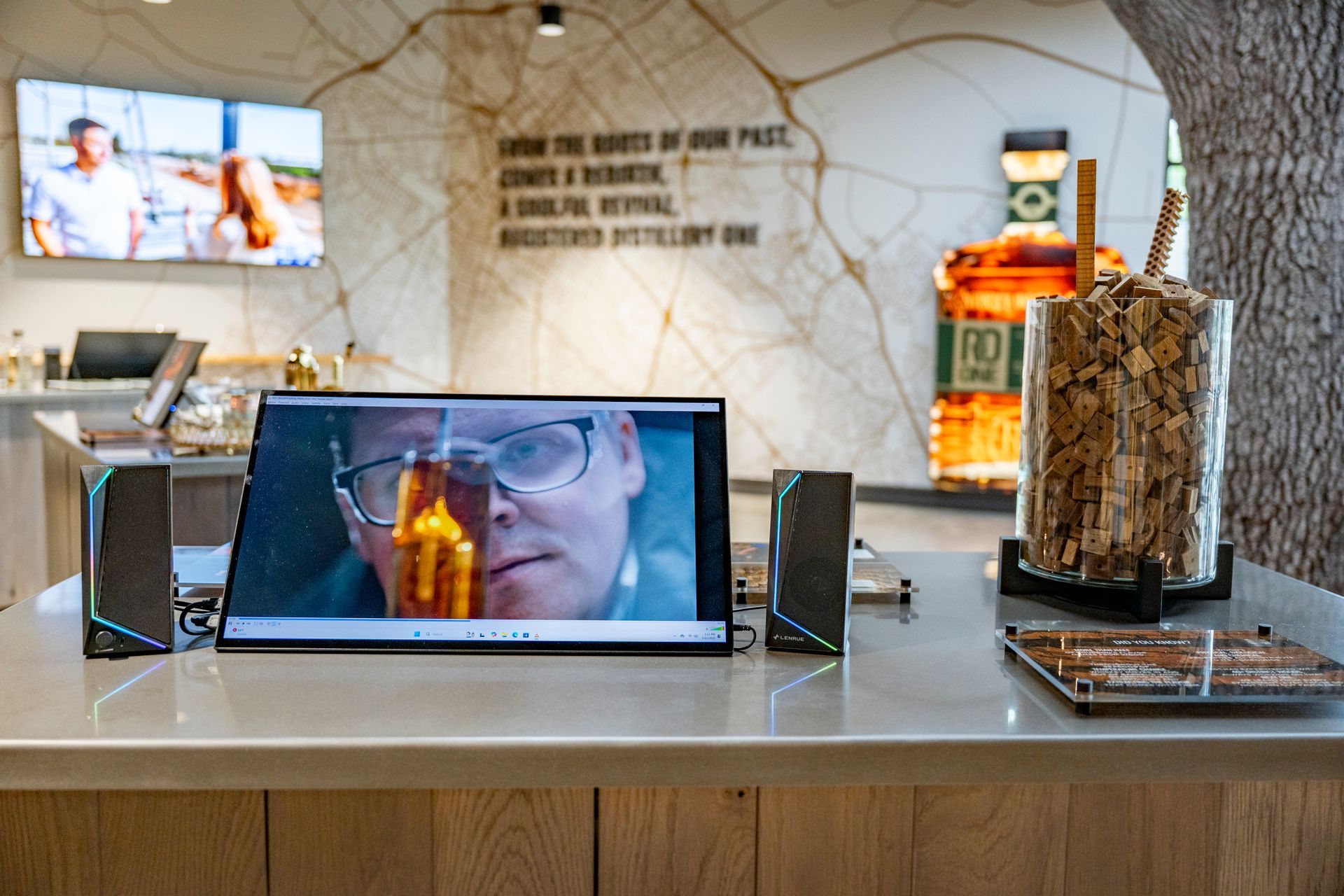 A retail counter with a video screen displaying a person. Two speakers flank the screen.