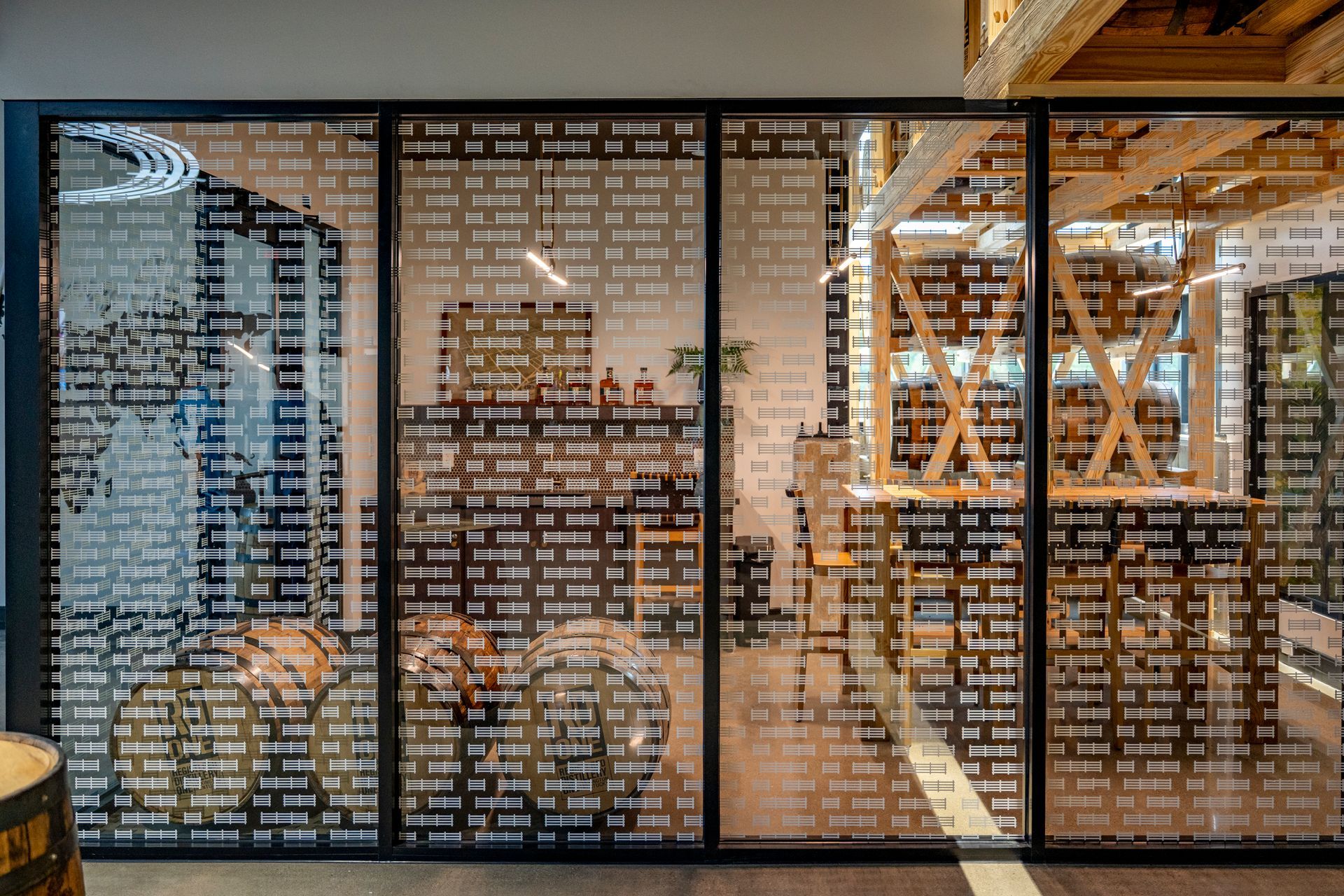 Glass partition with black metal frame and patterned cutouts, revealing a workspace.