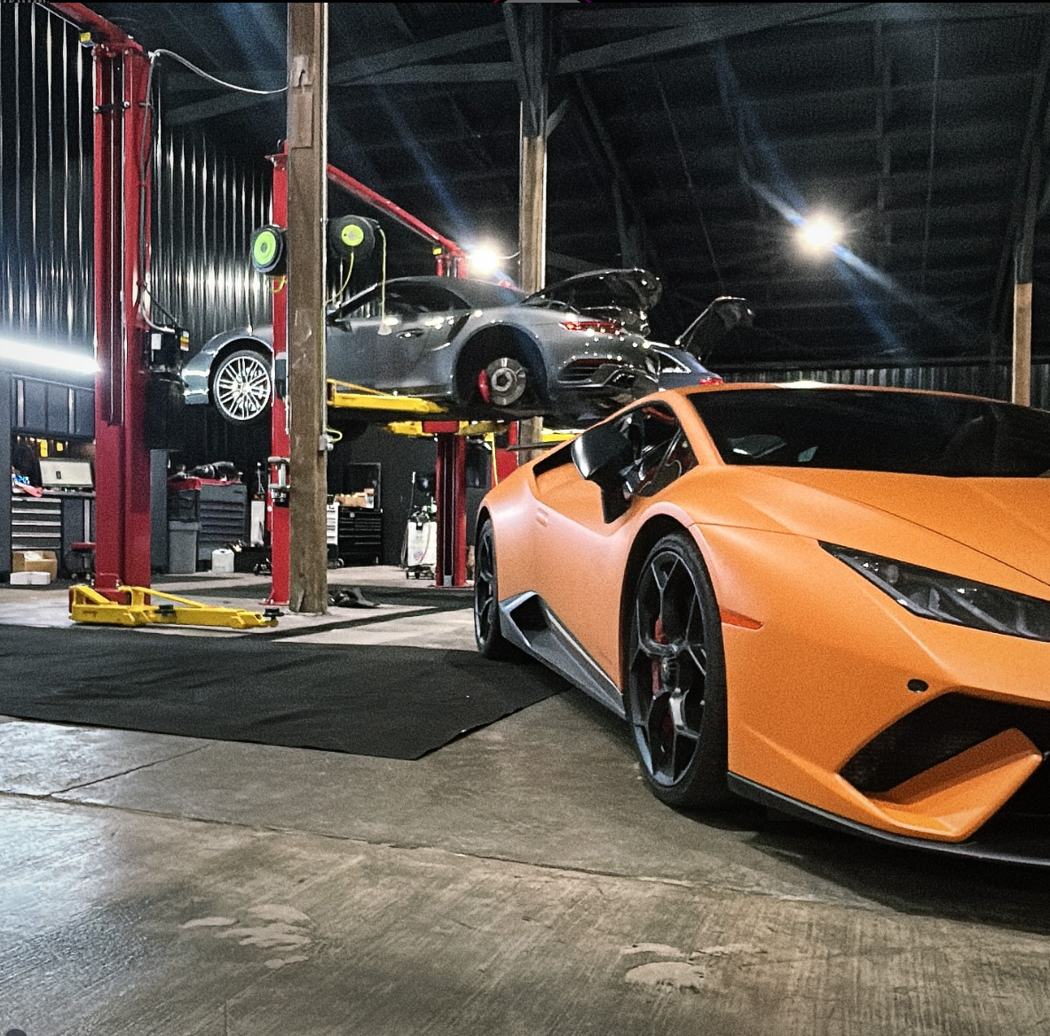 Orange Lamborghini in a garage with another car on a lift.