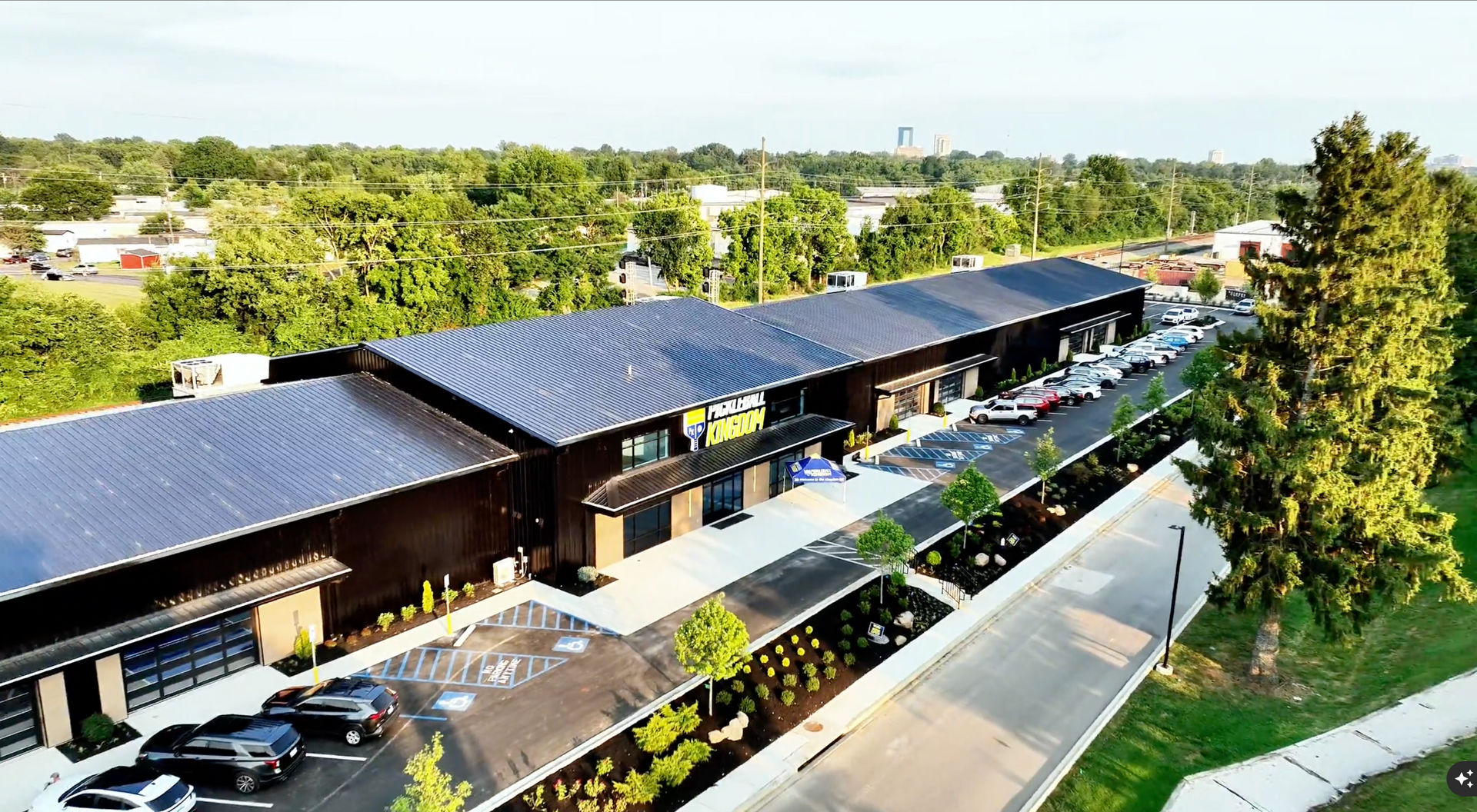 Aerial view of a modern building with solar panels on the roof, trees, and parked cars.