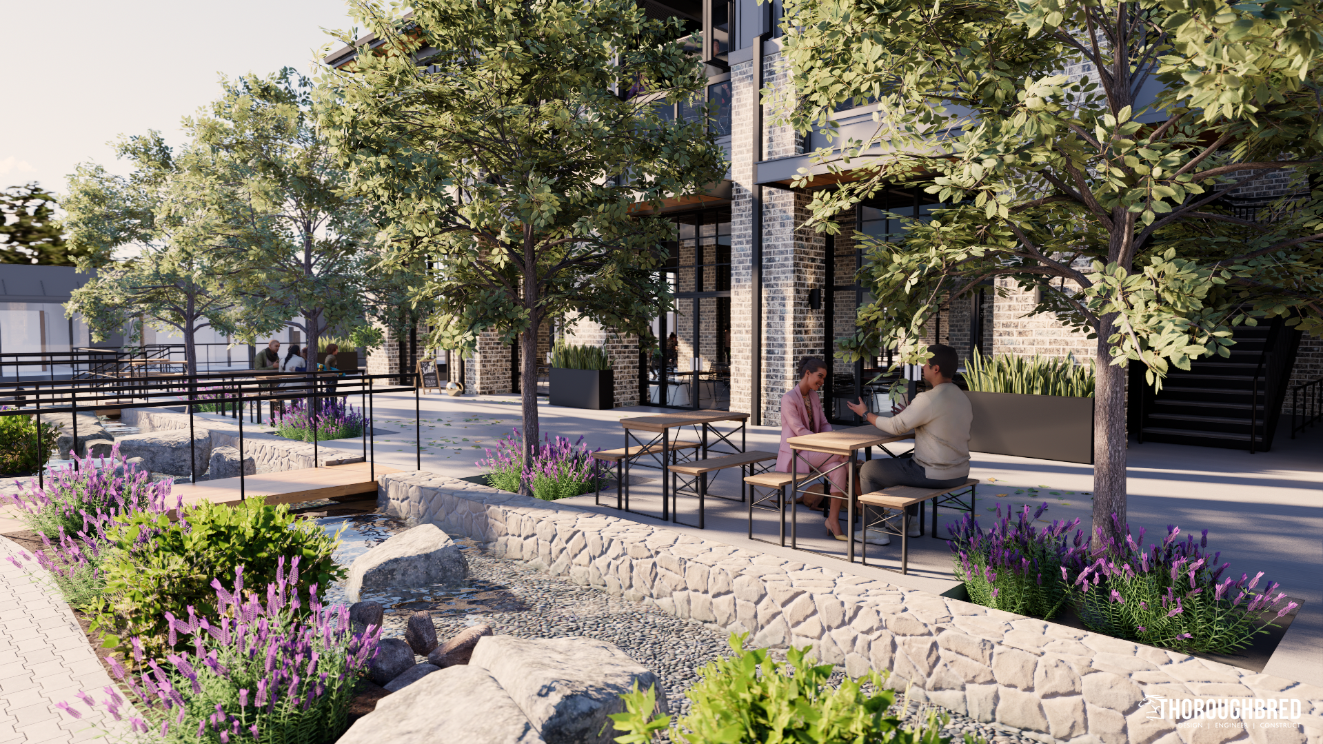 Outdoor cafe with stone walls, a stream, and tables. Two people sit at a table under a tree.