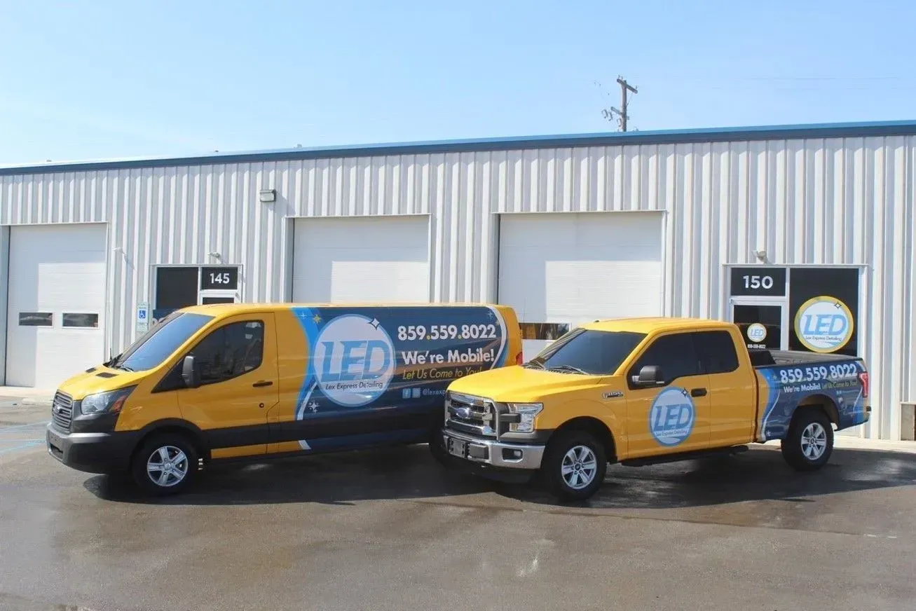 Yellow van and pickup truck with LEC logo parked in front of a white building with garage doors.
