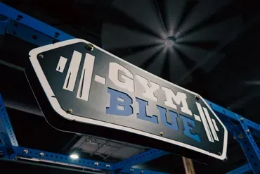 A sign for gym blue is hanging from the ceiling of a gym.