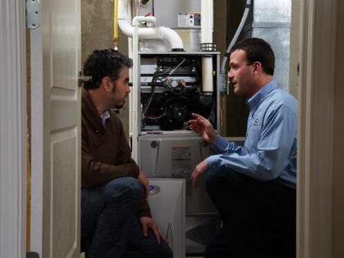 Two men examining a furnace in a utility closet. One gestures, explaining the unit.