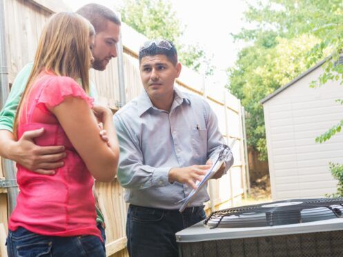 A couple consults with a service technician near an air conditioning unit outside.