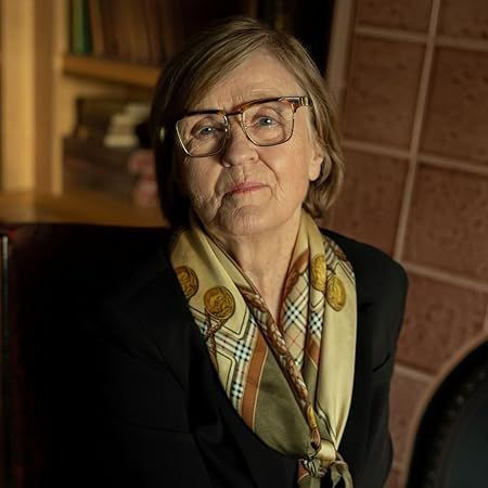 A woman wearing glasses and a scarf is sitting in a chair.