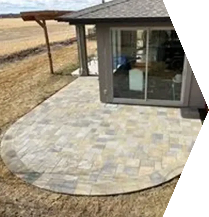 Stone patio beside a house with sliding glass doors, bordered by dry grass and an open landscape.