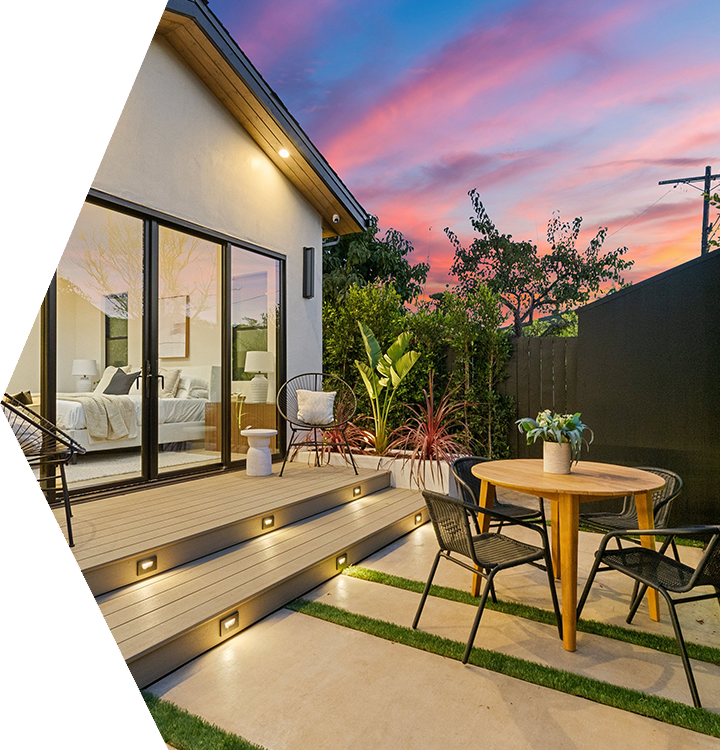 Modern patio beside a house at sunset, with outdoor seating, potted plants, and pink-blue sky. Modern patio beside a house at sunset, with outdoor seating, potted plants, and pink-blue sky.
