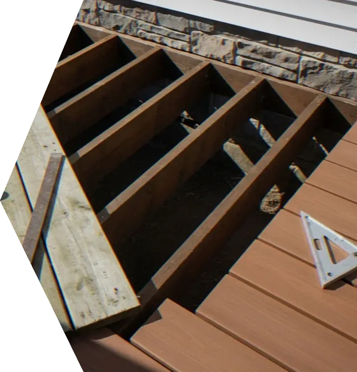 Wood deck framing with exposed joists beside stone siding and brown decking boards Wood deck framing with exposed joists beside stone siding and brown decking boards