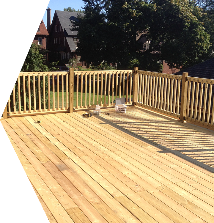 Sunlit wooden deck with railing, trees and houses in the background, and a few tools on the floor. Sunlit wooden deck with railing, trees and houses in the background, and a few tools on the floor.