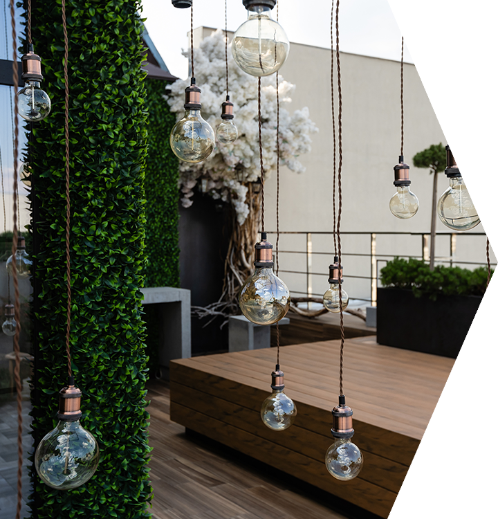 Outdoor terrace with hanging glass bulbs, a wooden deck, and lush green wall decor Outdoor terrace with hanging glass bulbs, a wooden deck, and lush green wall decor