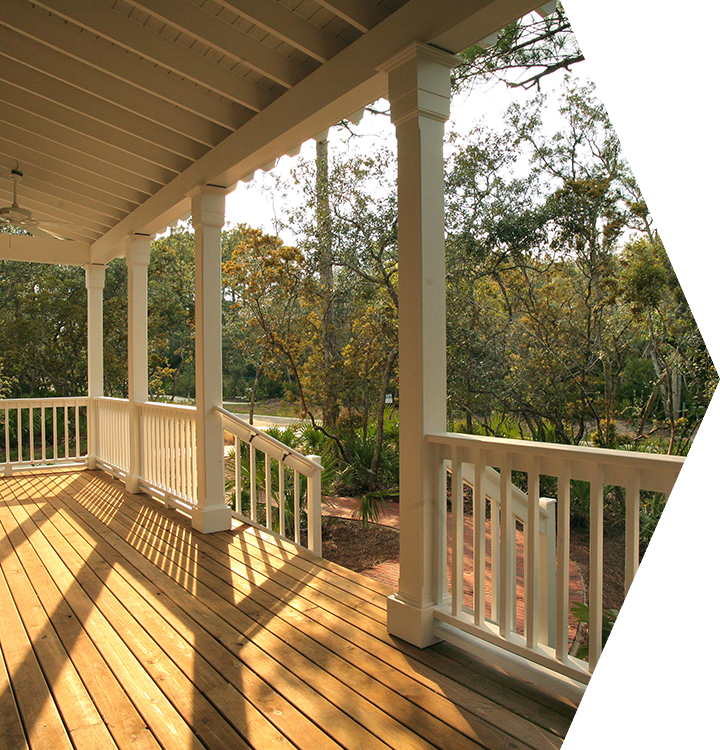 Sunlit wooden porch with white railings overlooking trees and a wooded yard Sunlit wooden porch with white railings overlooking trees and a wooded yard