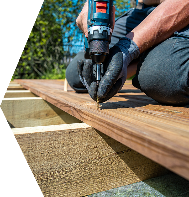 Gloved hands use a drill to drive a screw into a wooden deck board outdoors Gloved hands use a drill to drive a screw into a wooden deck board outdoors