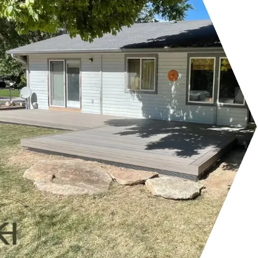 Backyard deck with sliding glass doors on a white house, bordered by large rocks and dry grass.