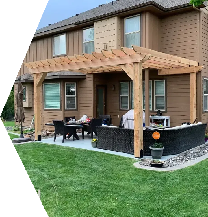 Backyard patio with wooden pergola, black wicker furniture, and a two-story house behind it