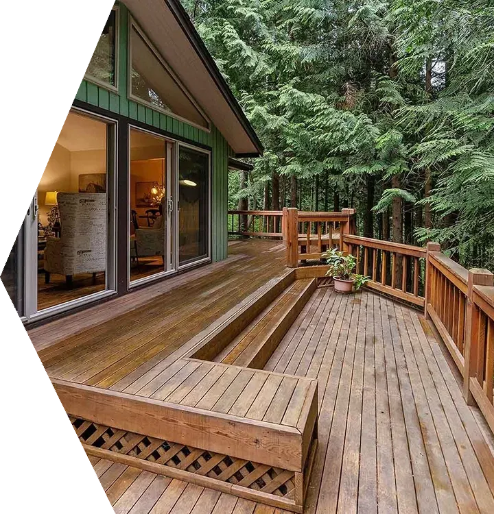 Wooden deck beside a cabin, surrounded by tall green trees and railings.