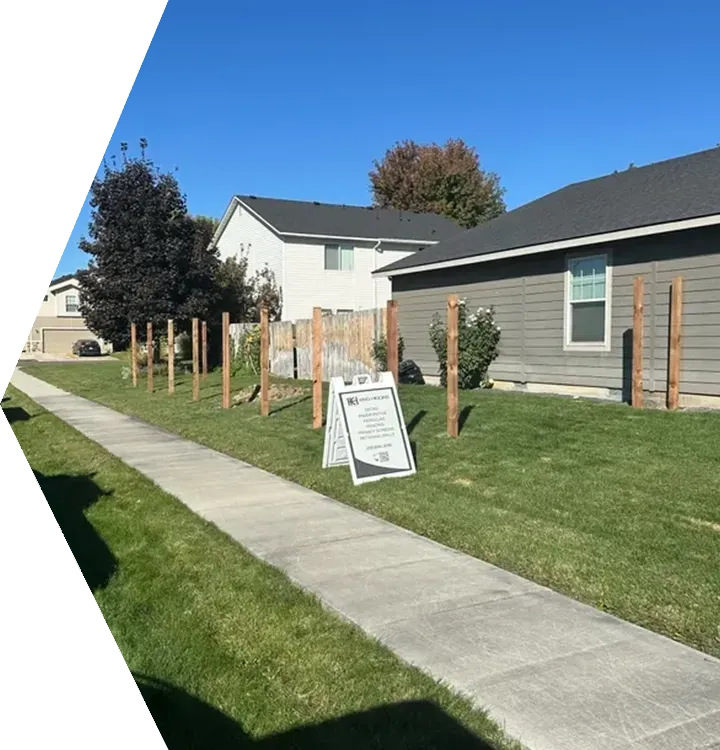 Residential yard with newly planted wooden posts and a yard sign beside a sidewalk on a sunny day Residential yard with newly planted wooden posts and a yard sign beside a sidewalk on a sunny day