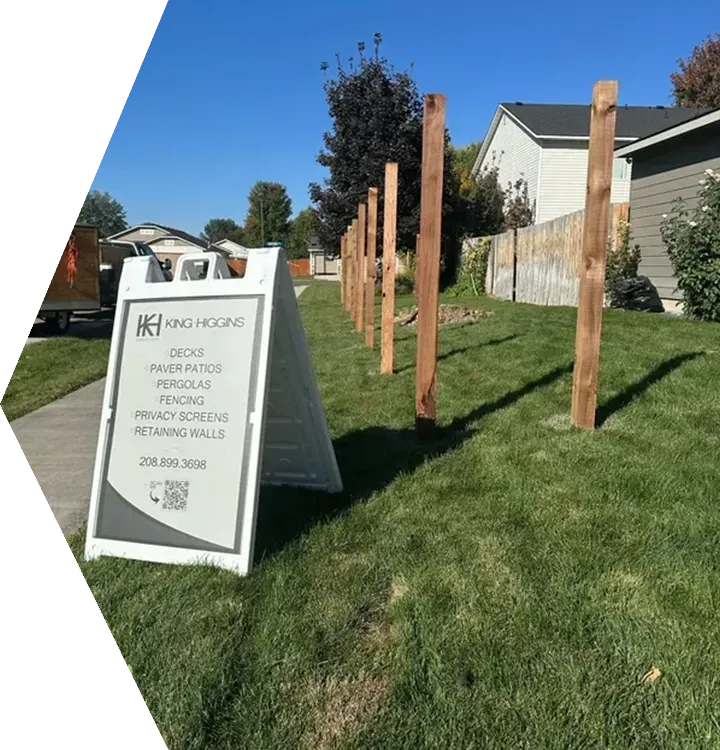 Yard sign for a home construction project beside a grassy lawn with wooden posts and houses in the background Yard sign for a home construction project beside a grassy lawn with wooden posts and houses in the background