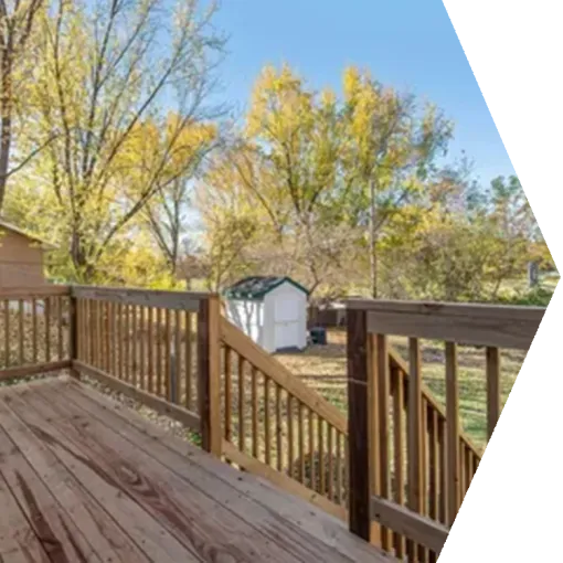 Wooden deck with railing overlooking a backyard and white shed amid autumn trees