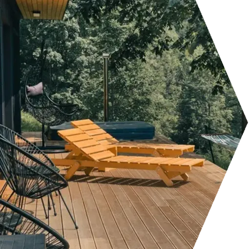 Wooden deck with orange lounge chairs and black seating overlooking a lush green forest.