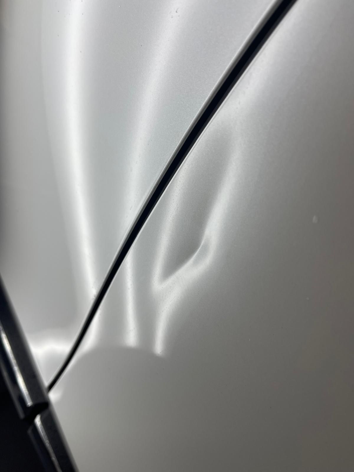 Silver car door with a large dent.