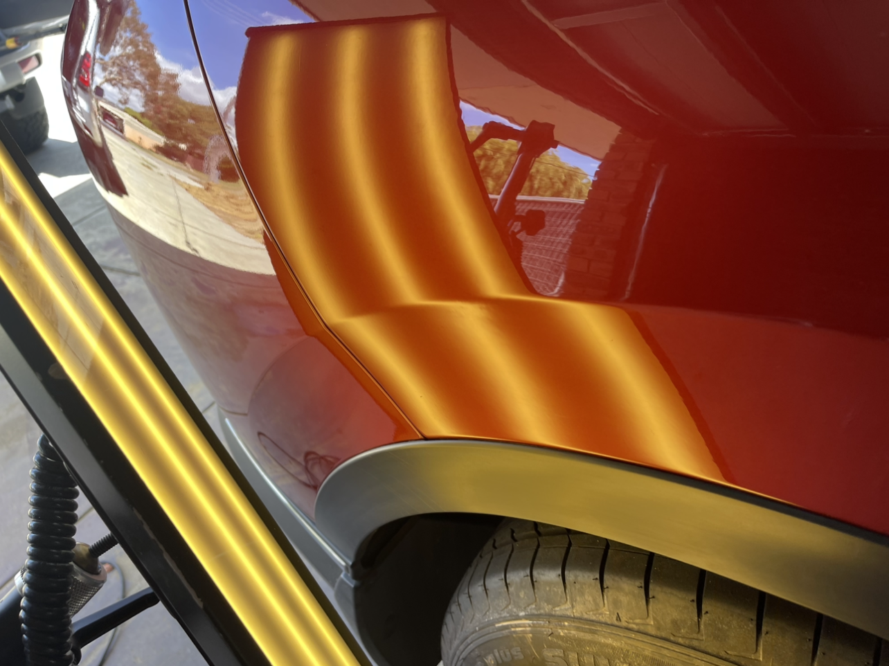 Red car body with a large dent being repaired, reflecting light and surroundings.