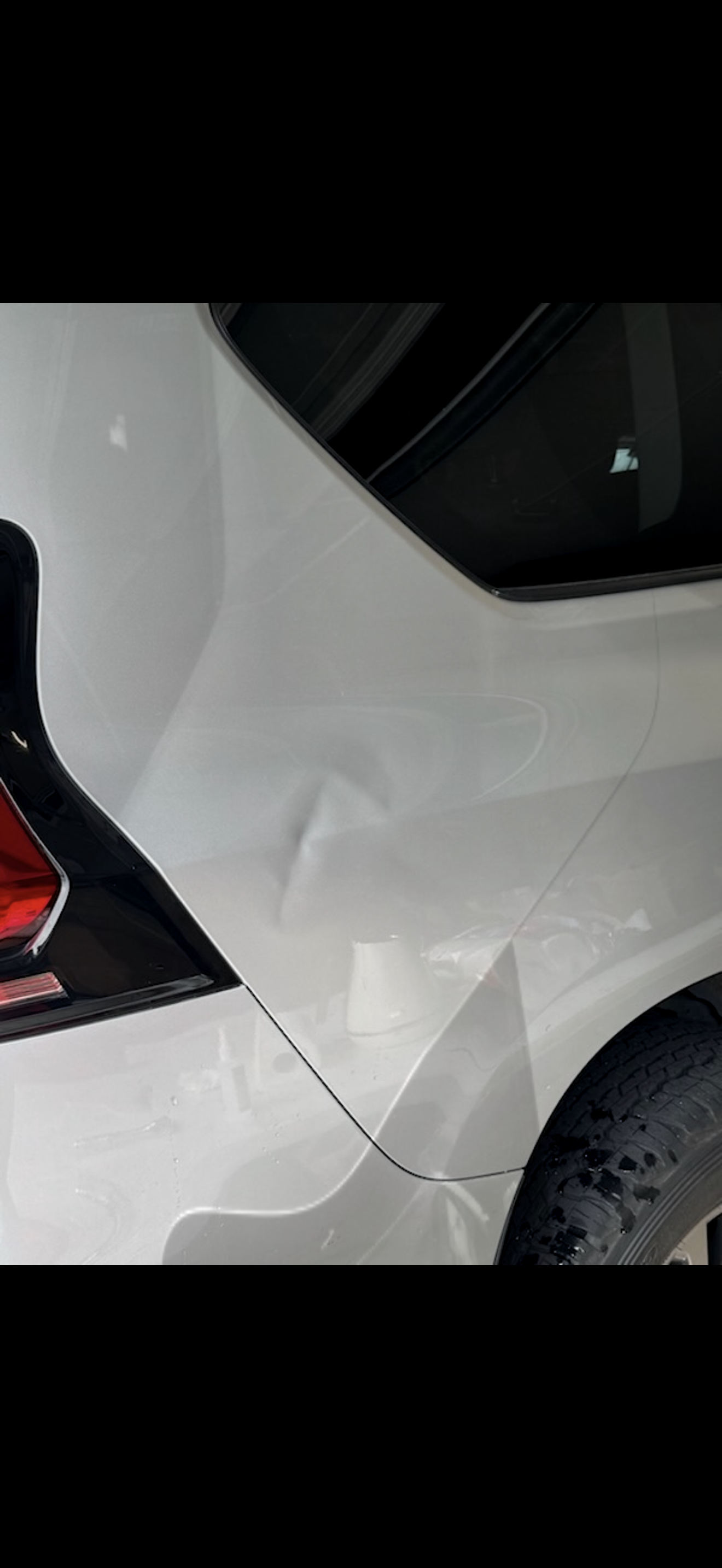 White car's rear side with a dent, likely from a collision, showing damage and a crack in the paint.