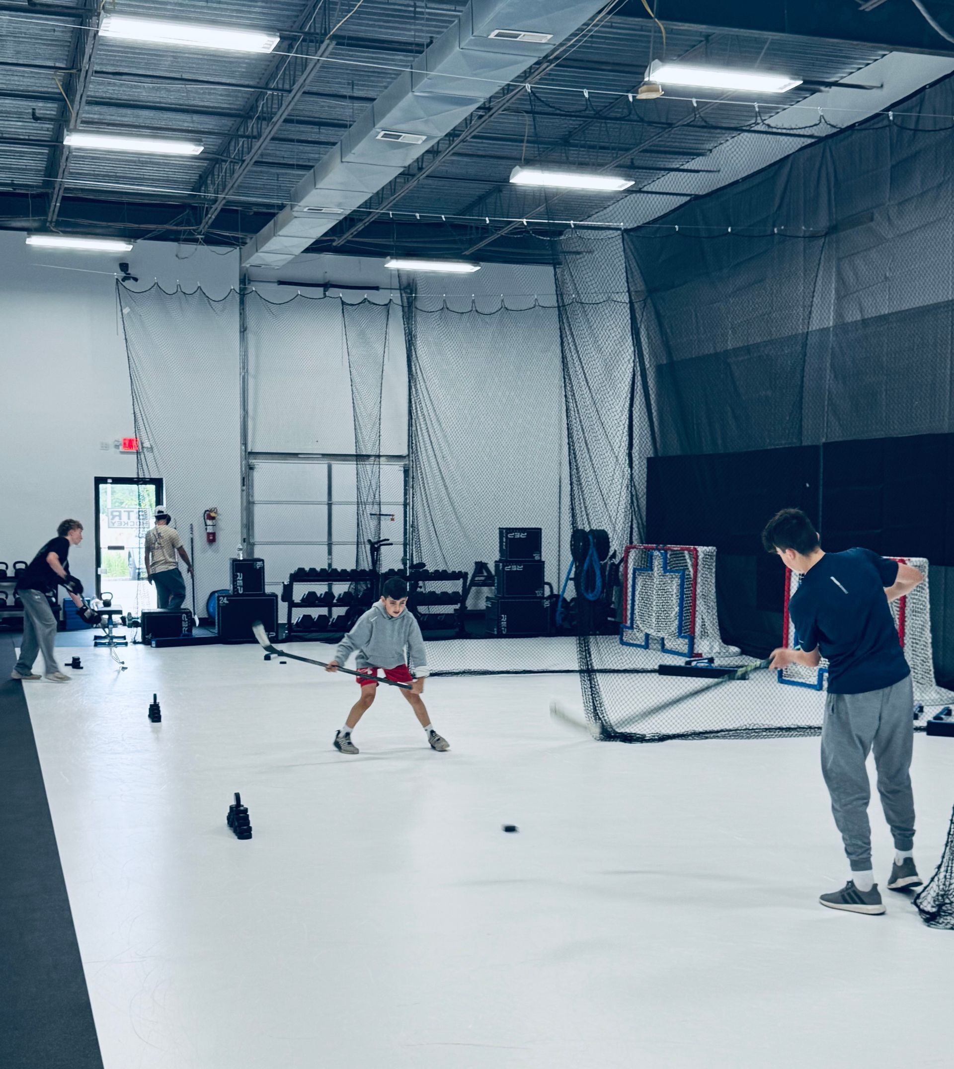 People practicing indoor golf in a large netted training facility