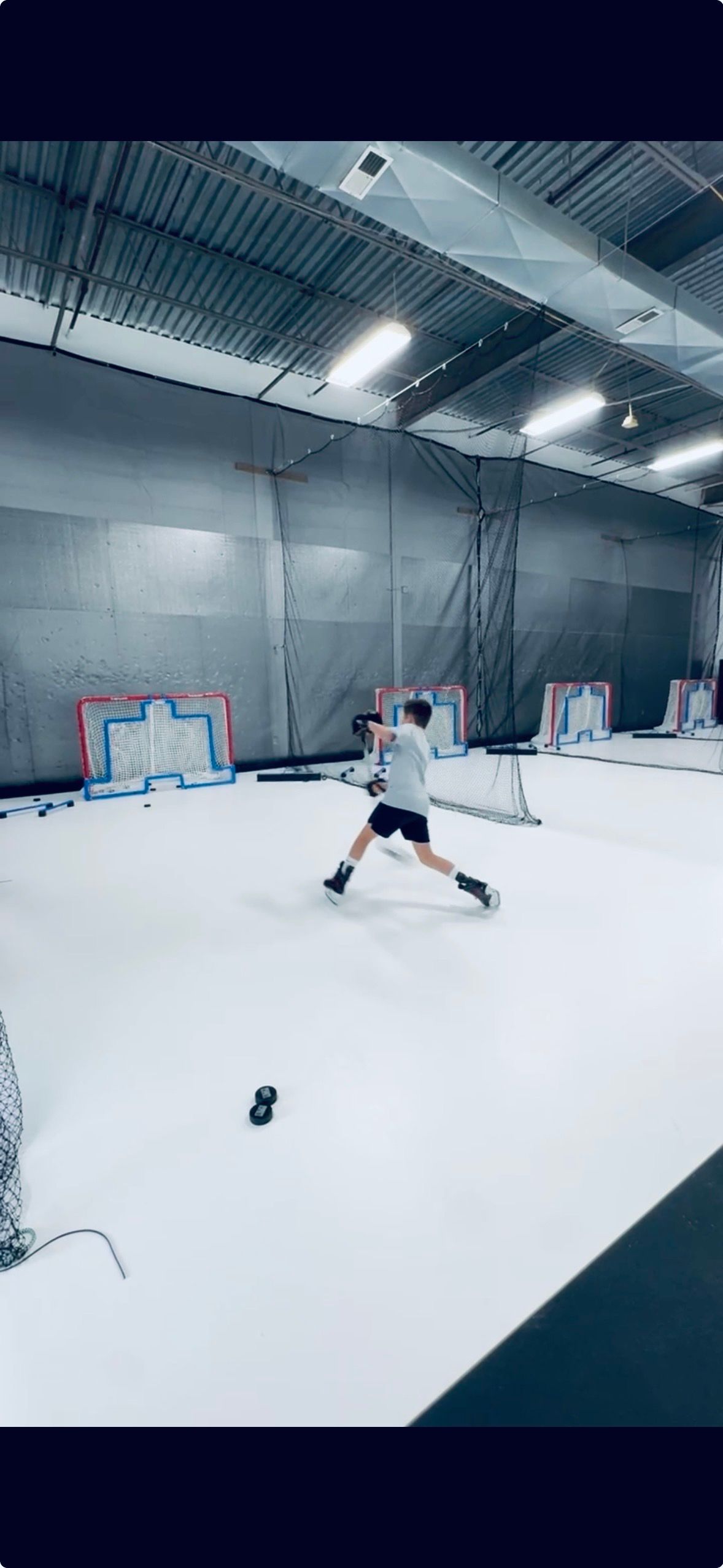 Person skiing indoors on an artificial snow slope with nets and lights overhead