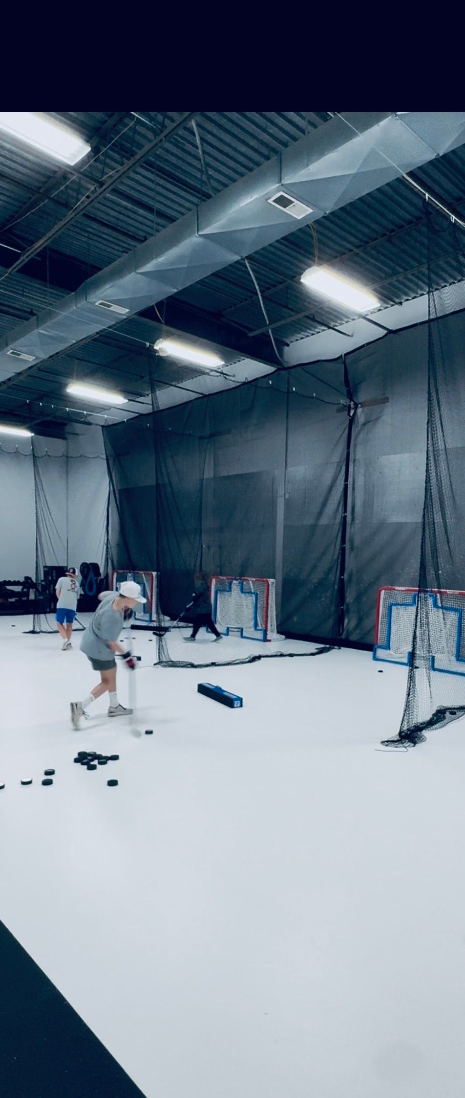Indoor sports facility with white floor, netted walls, and a few people practicing near equipment