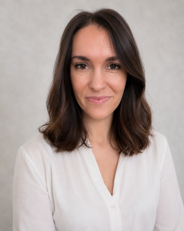 Portrait of a smiling woman with shoulder-length dark hair wearing a white blouse against a gray background