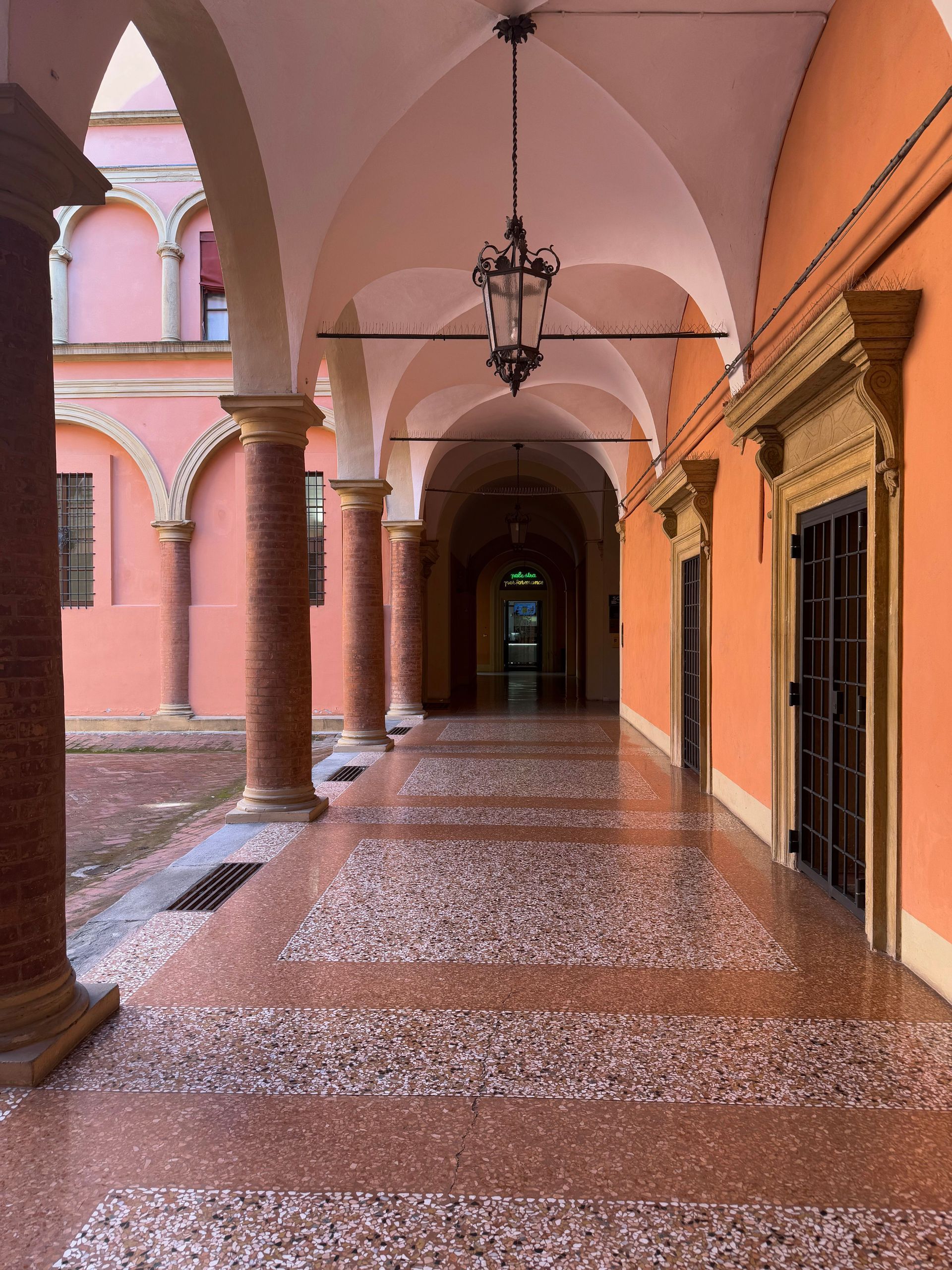 Arched pink colonnade with hanging lanterns and patterned tiled floor in a covered courtyard