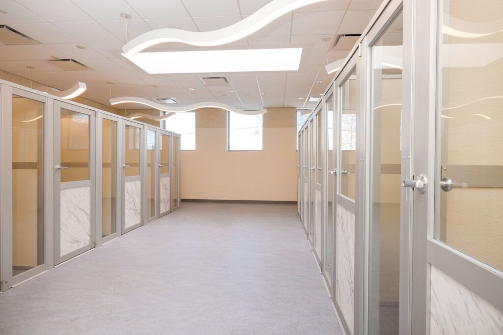 Empty office hallway with glass-walled cubicles and beige carpet under bright ceiling lights