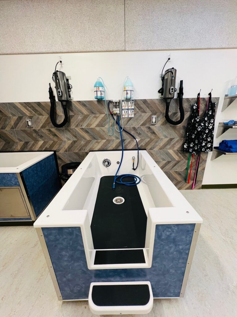 Pet grooming tub with hose sprayers, towels, and a non-slip step in a grooming station