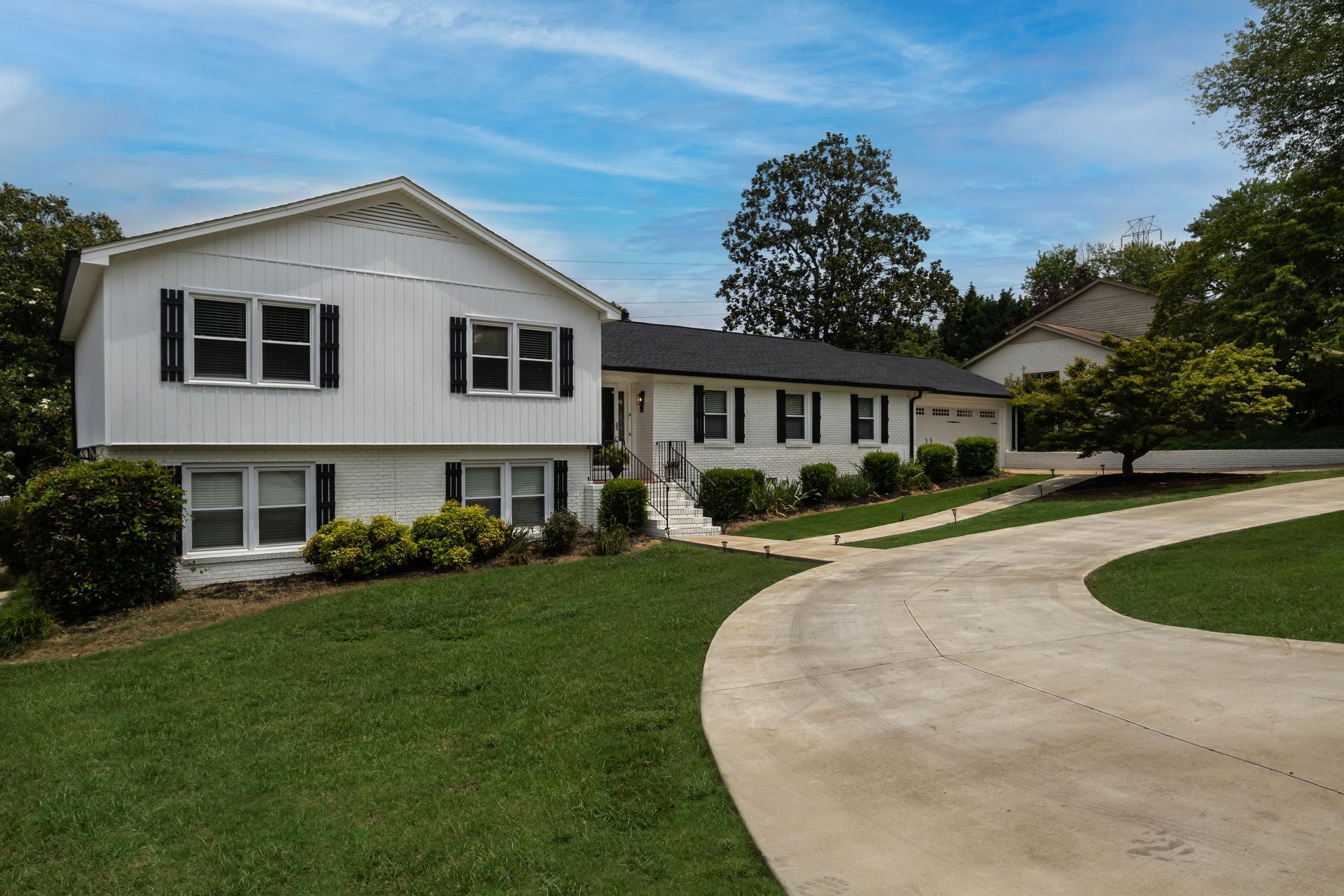 Suburban white house with a curved driveway, green lawn, and trees under a blue sky