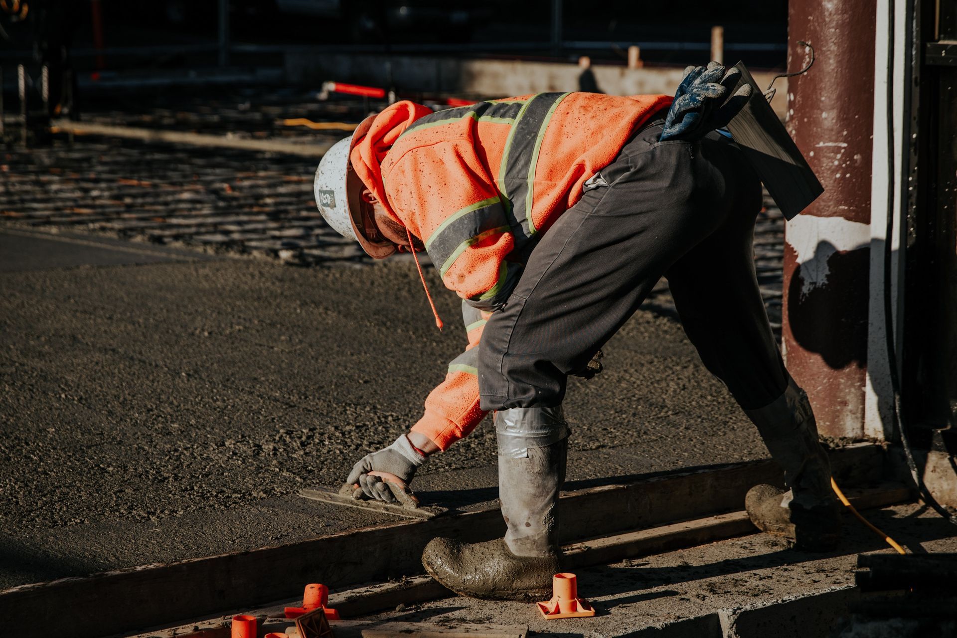 Worker in orange safety vest bending over railway tracks at night, using a tool near the rails.